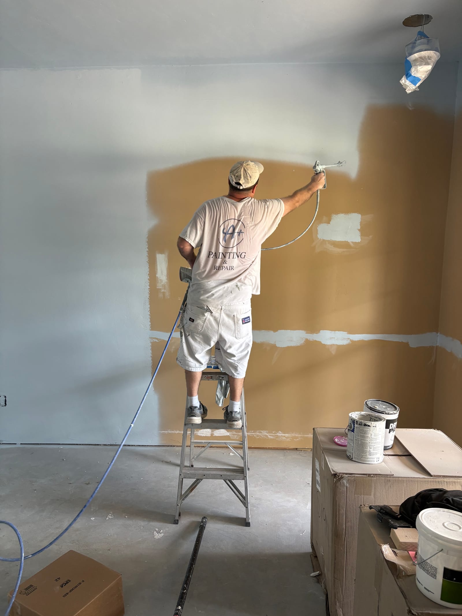 Chris on a step ladder painting up near the ceiling line, fresh white over drywall prep