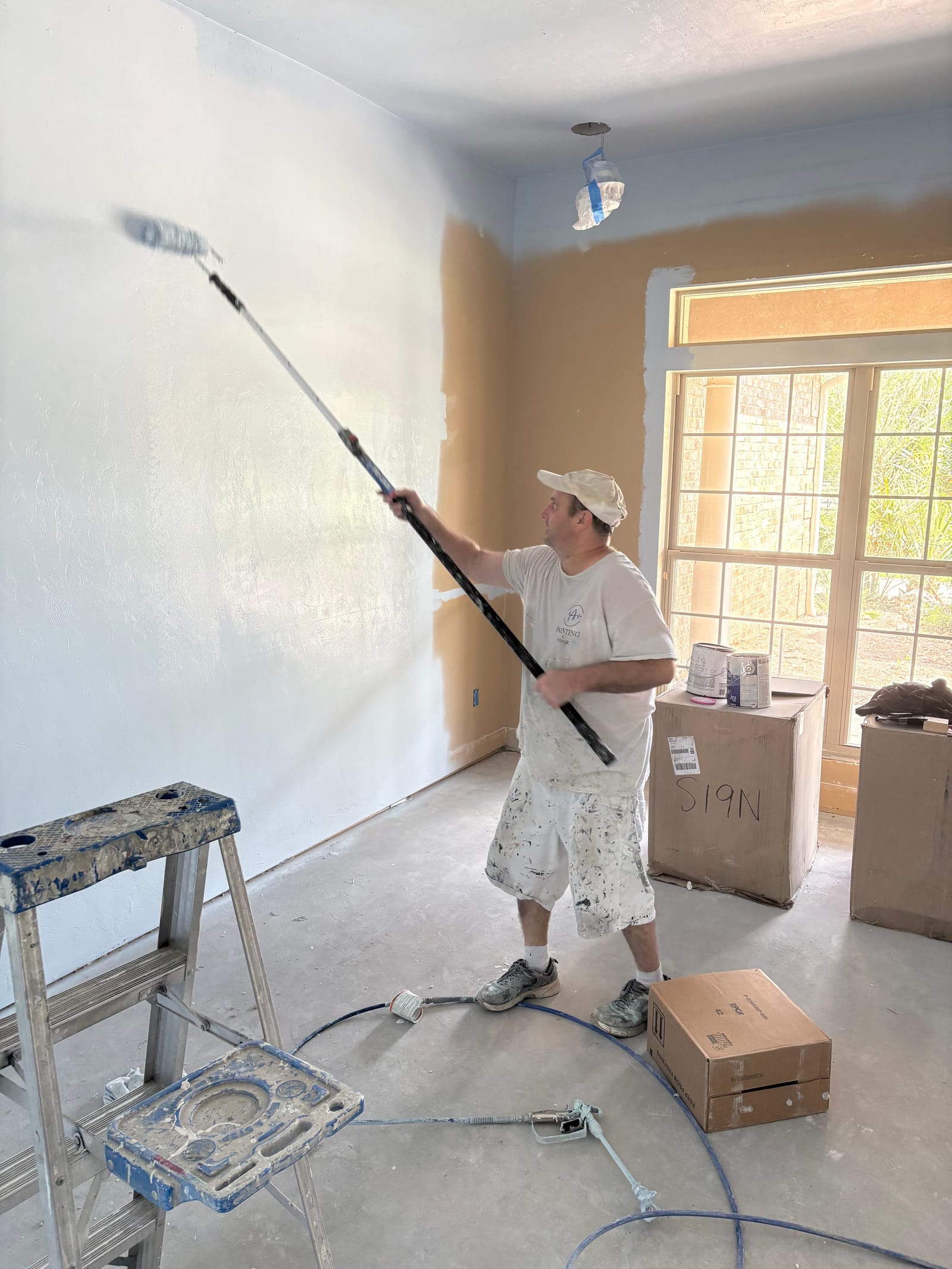 Chris with an extension-pole roller laying down an even coat on a partially painted interior wall