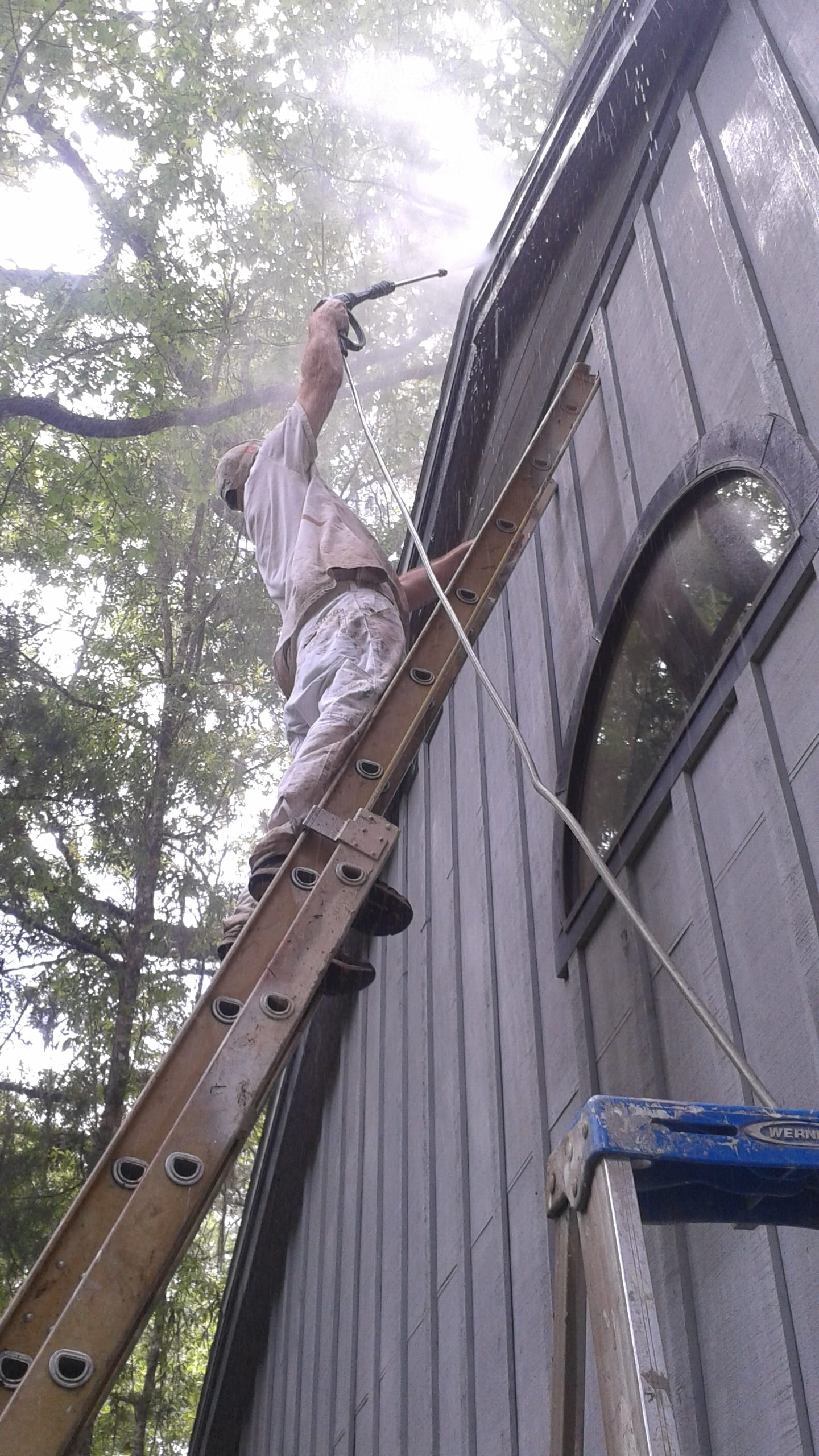 Christopher Combs on a ladder pressure washing a home before paint
