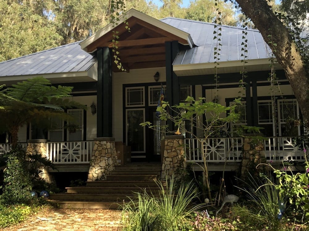 Completed porch home with white siding, dark trim, restored amber wood beams, and metal roof
